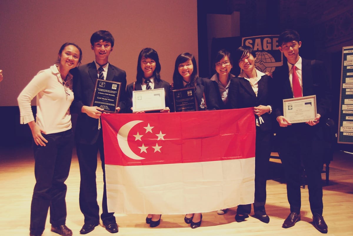 Students and mentors holding the Singapore flag and award plaques on stage at the SAGE World Cup 2011.